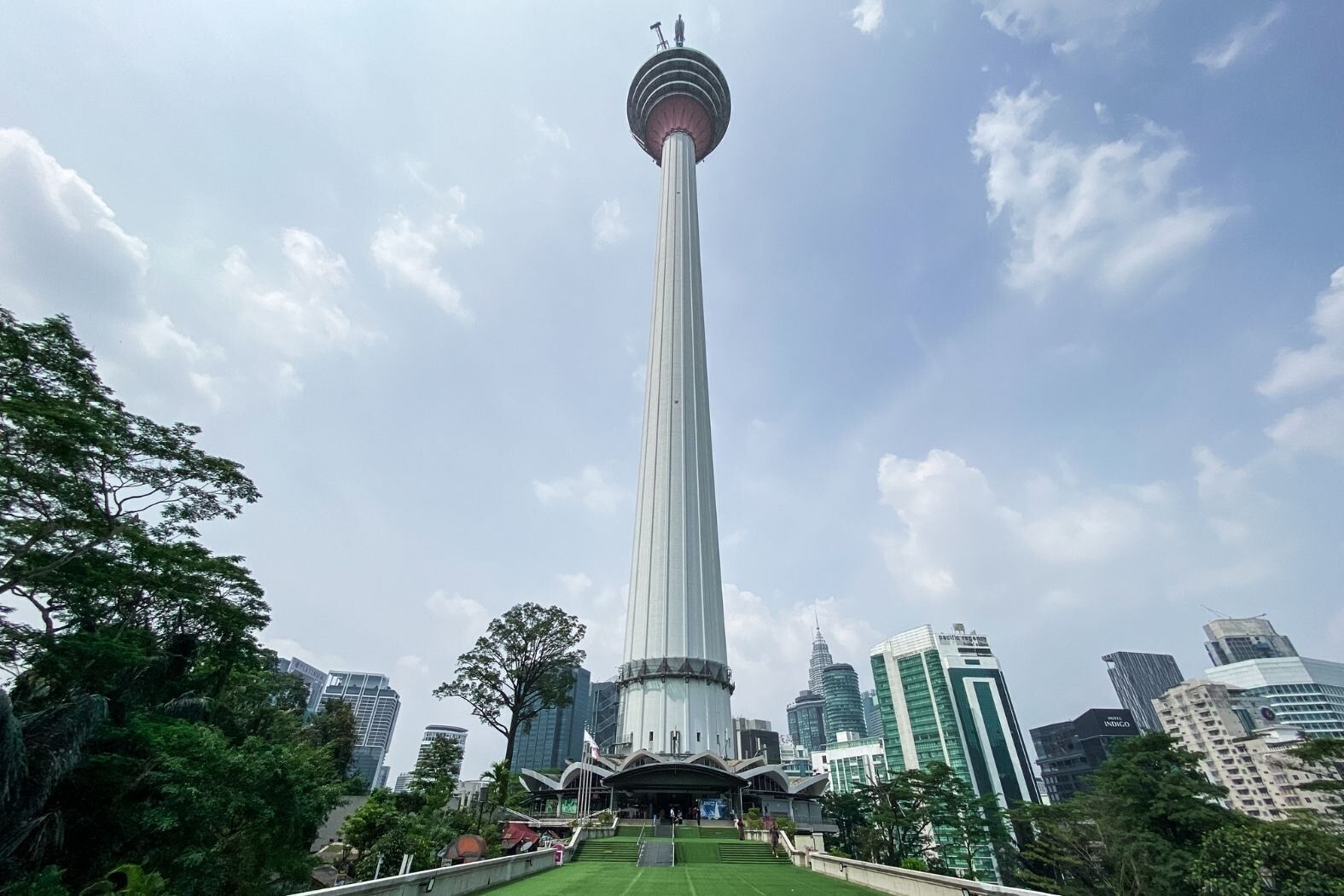 A tall tower with a circular observation deck, surrounded by modern buildings and greenery.