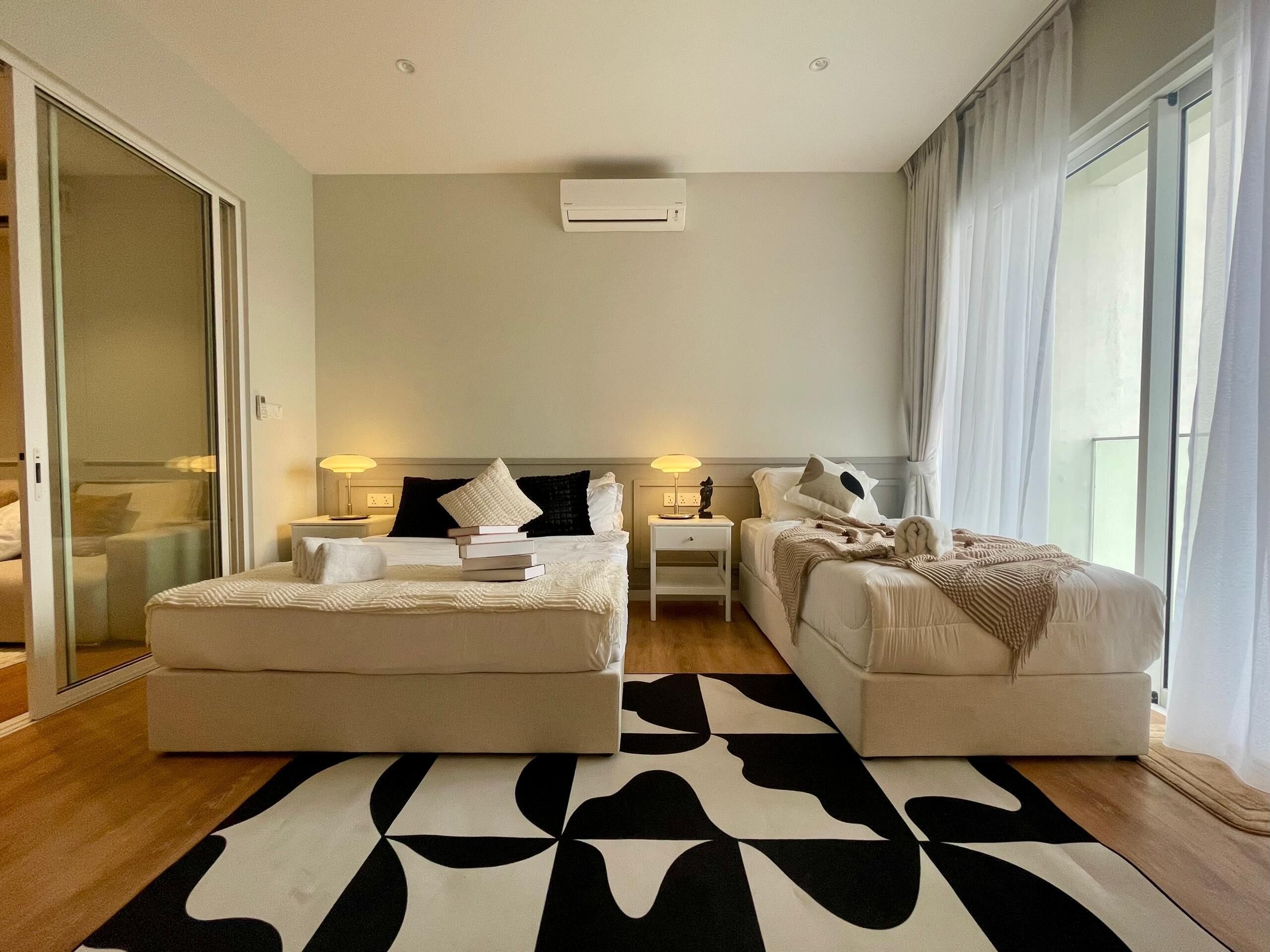 Habitación de hotel moderna con una cama grande, dos mesitas de noche, un sofá y un ventanal con cortinas.