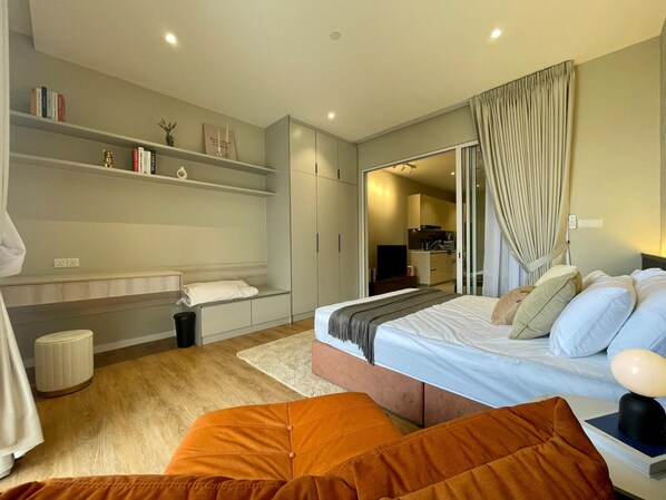 Quarto moderno com cama, área de estar, estante e banheiro visível através de uma porta aberta.