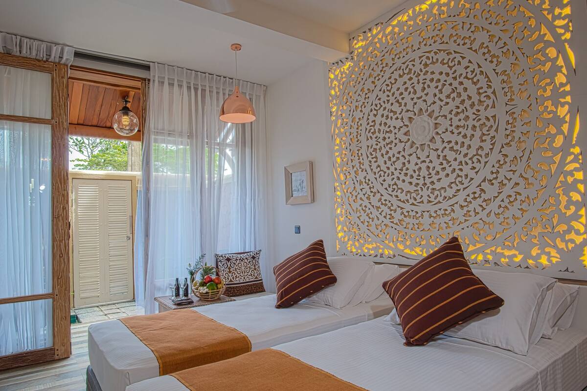 A bedroom with two beds, a decorative wall panel, and a window with curtains.