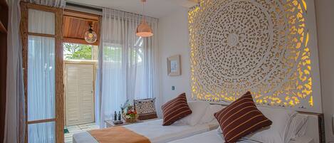A bedroom with two beds, a decorative wall panel, and a window with curtains.