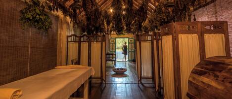 A traditional spa room with wooden benches, a central fire pit, and hanging plants.