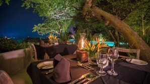 An outdoor dining table set with plates, cutlery, and a candle, surrounded by greenery and overlooking a pool. - Lady Hill Hotel (Galle)