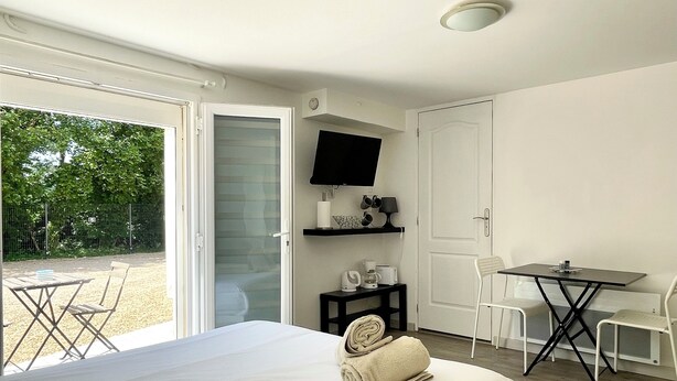 Un dormitorio con cama, escritorio, silla, televisor y balcón con mesa y sillas.