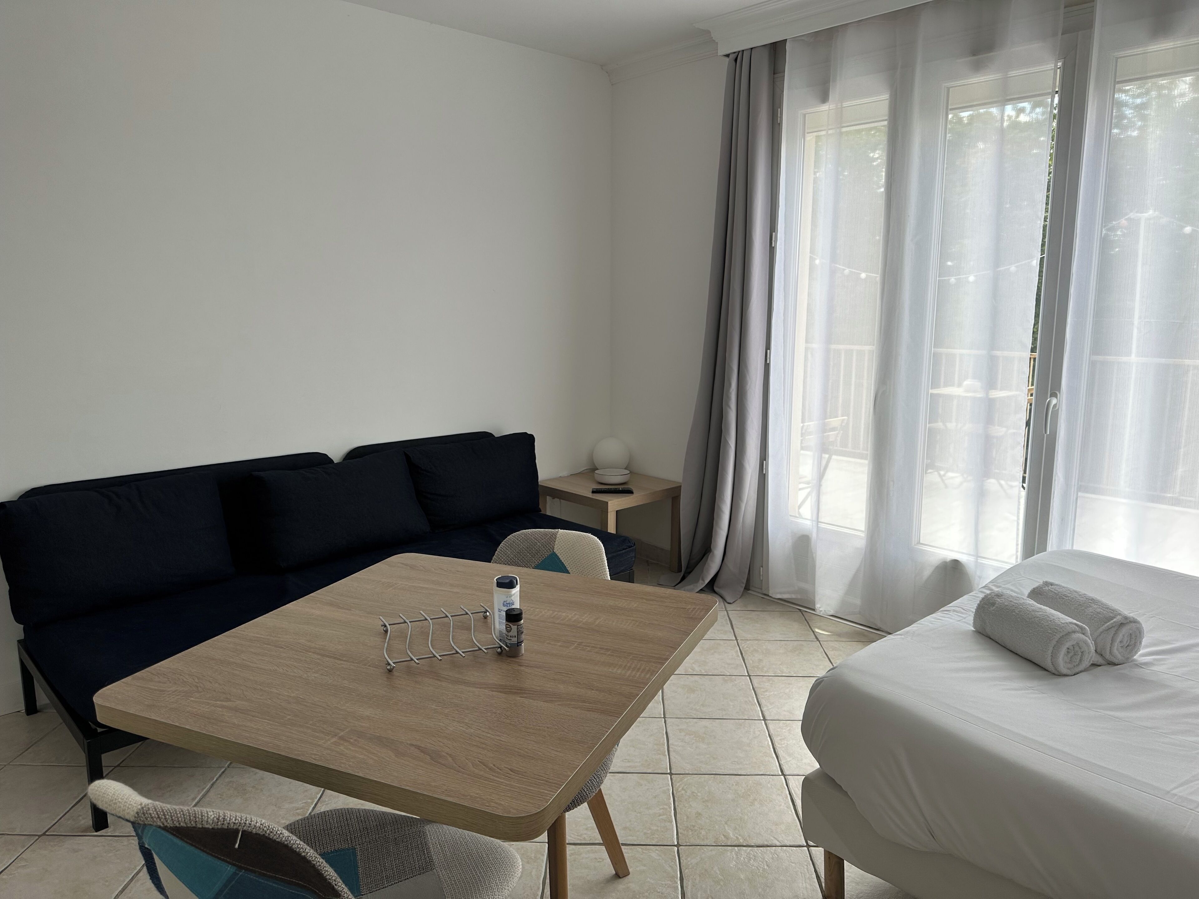 A hotel room with a bed, a sofa, a table with a bottle, and a chair.