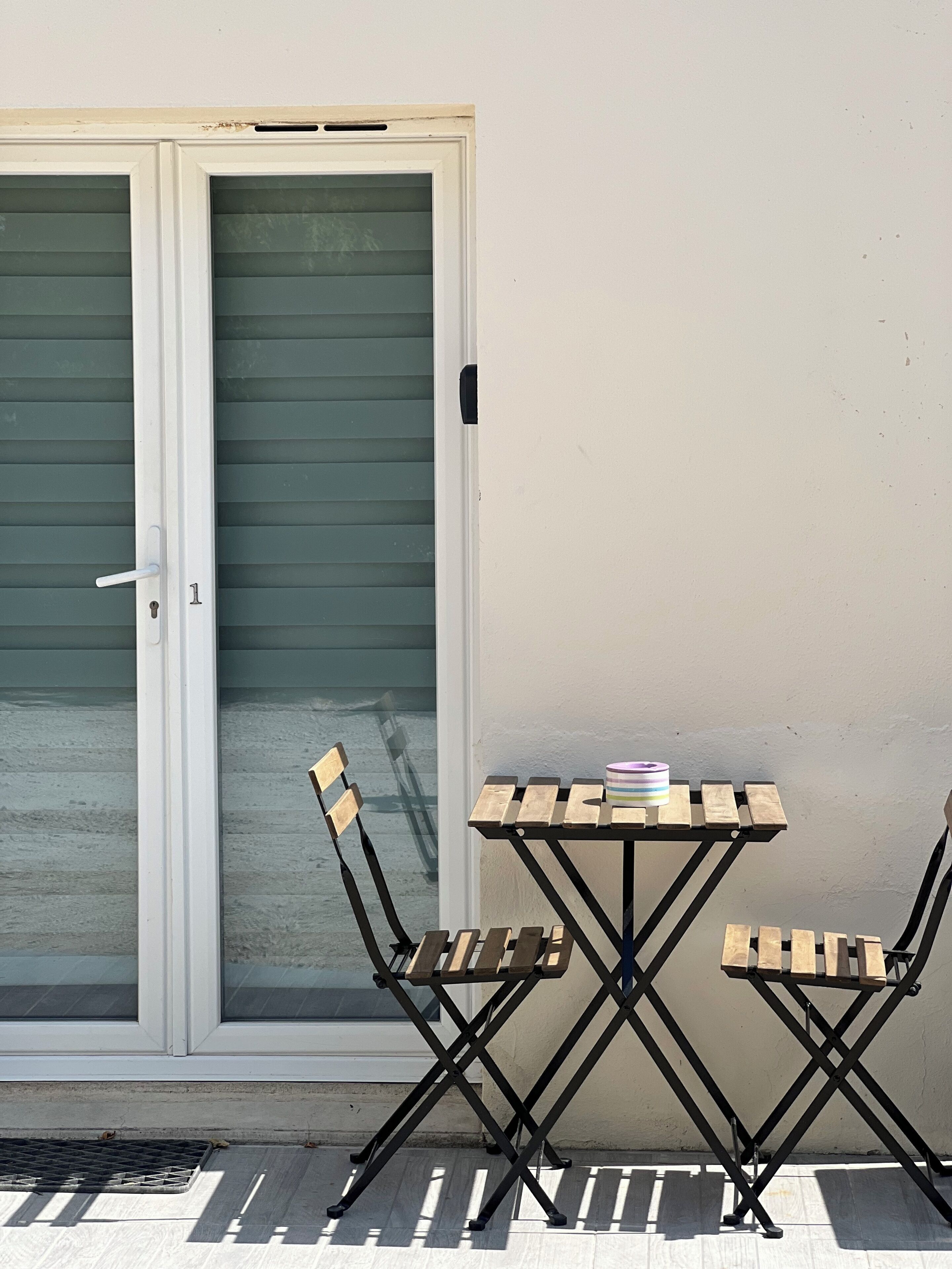 Una porta a vetri scorrevoli con maniglia in metallo, un tavolino con un contenitore a righe e due sedie in legno.