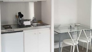 Cocina compacta con armarios blancos, un microondas y un comedor con mesa de vidrio y sillas blancas.