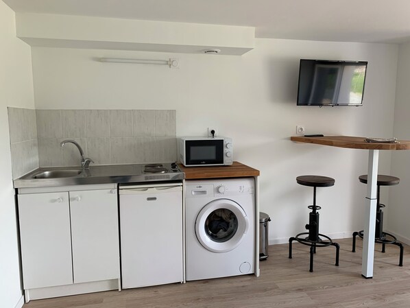 Cocina compacta con lavadora, microondas, fregadero y una pequeña mesa con taburetes.