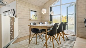 A modern dining area with a wooden table, black chairs, and a large window providing a view of the outdoors. - Amazing home in Tarm with sauna (Tarm)