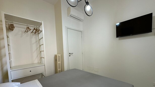 A bedroom with a bed, a wardrobe with clothes, a radiator, a door, and a TV on the wall. - Bed&BikeRome ANGELICO  (Rome)