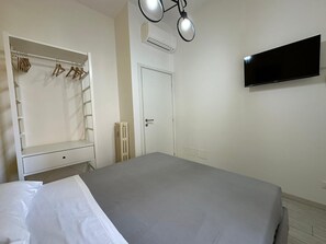 A bedroom with a bed, a wardrobe with clothes, a radiator, a door, and a TV on the wall. - Bed&BikeRome ANGELICO  (Rome)