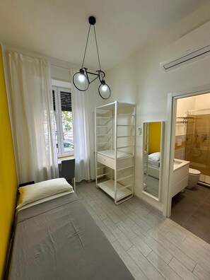 Un dormitorio moderno con cama, un armario blanco, un baño con ducha y una ventana con cortinas.