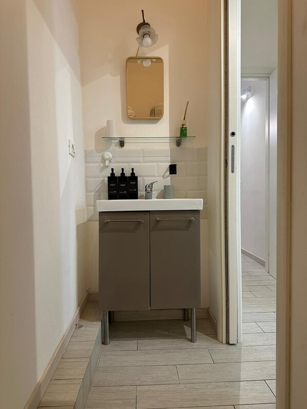 A modern bathroom with a white sink, grey cabinets, and a mirror above. - Bed&BikeRome ANGELICO (Rome)