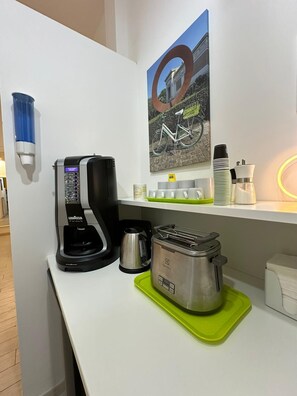 Una kitchenette equipada con cafetera, tostadora, hervidor y un cuadro con una bicicleta en la pared.