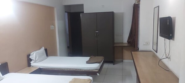A bedroom with two beds, a wardrobe, a TV, and a bathroom visible through an open door. - Ozone Guest House (Pune)