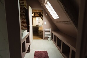 A narrow hallway with a sloped ceiling, a radiator, and a window.
