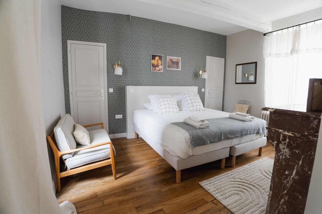 Een slaapkamer met een bed, een stoel, een nachtkastje en een raam met gordijnen.