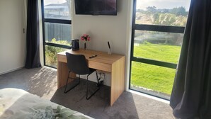 A hotel room with a wooden desk, a chair, a TV mounted on the wall, and large windows with curtains. - A Gem In Ascot is situated in Invercargill. (Invercargill)