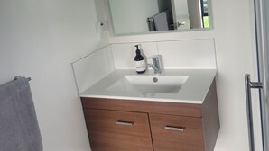 A modern bathroom with a white vanity, a large mirror, and a grey towel. - A Gem In Ascot is situated in Invercargill. (Invercargill)