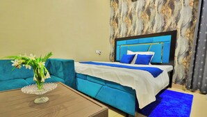 Una camera d'albergo con un letto, un divano blu, un tavolino da caffè con un vaso di fiori e una parete con motivi marmorizzati.