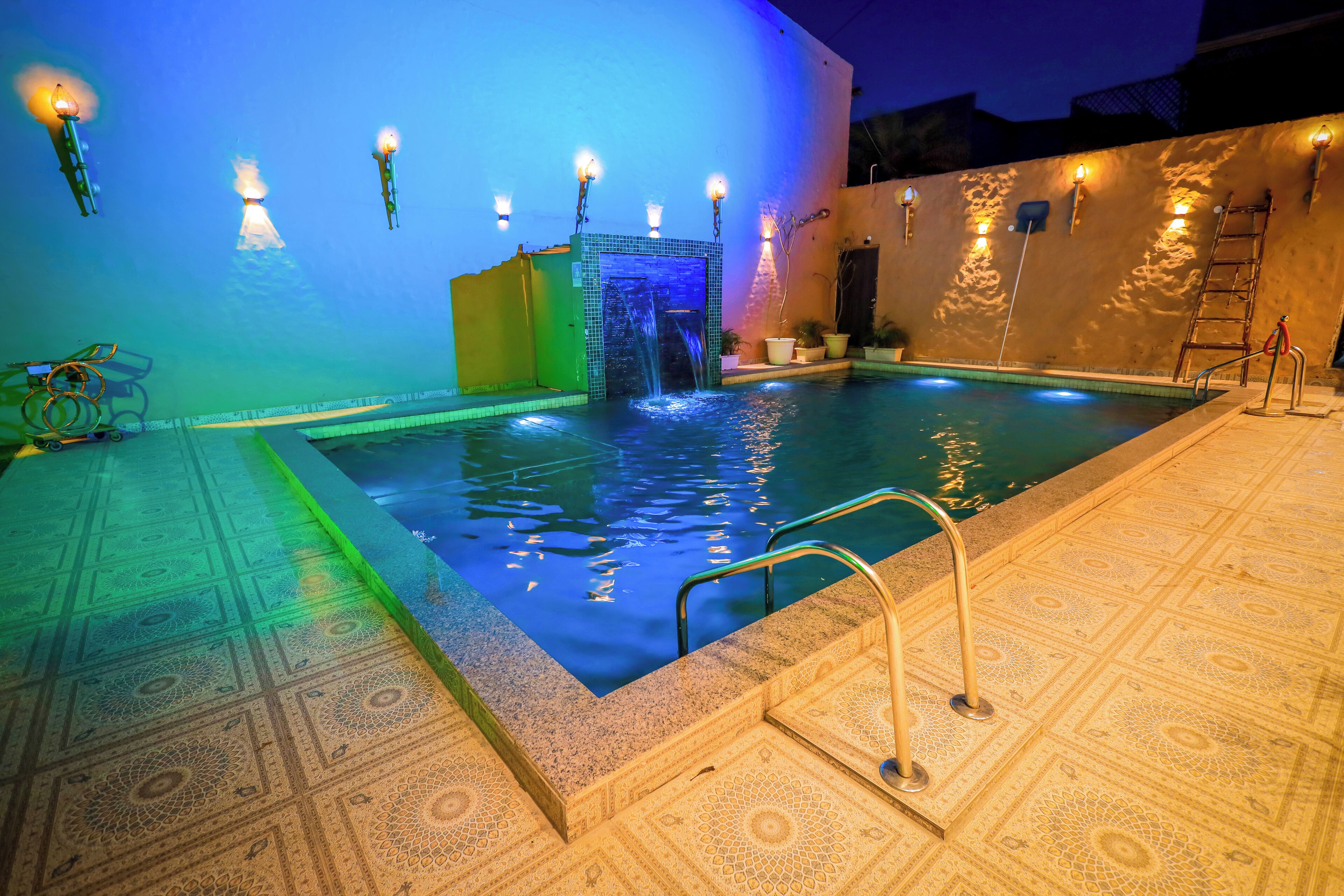 Una piscina con elemento d'acqua, circondata da pavimento e pareti decorate, illuminata da luci a parete.