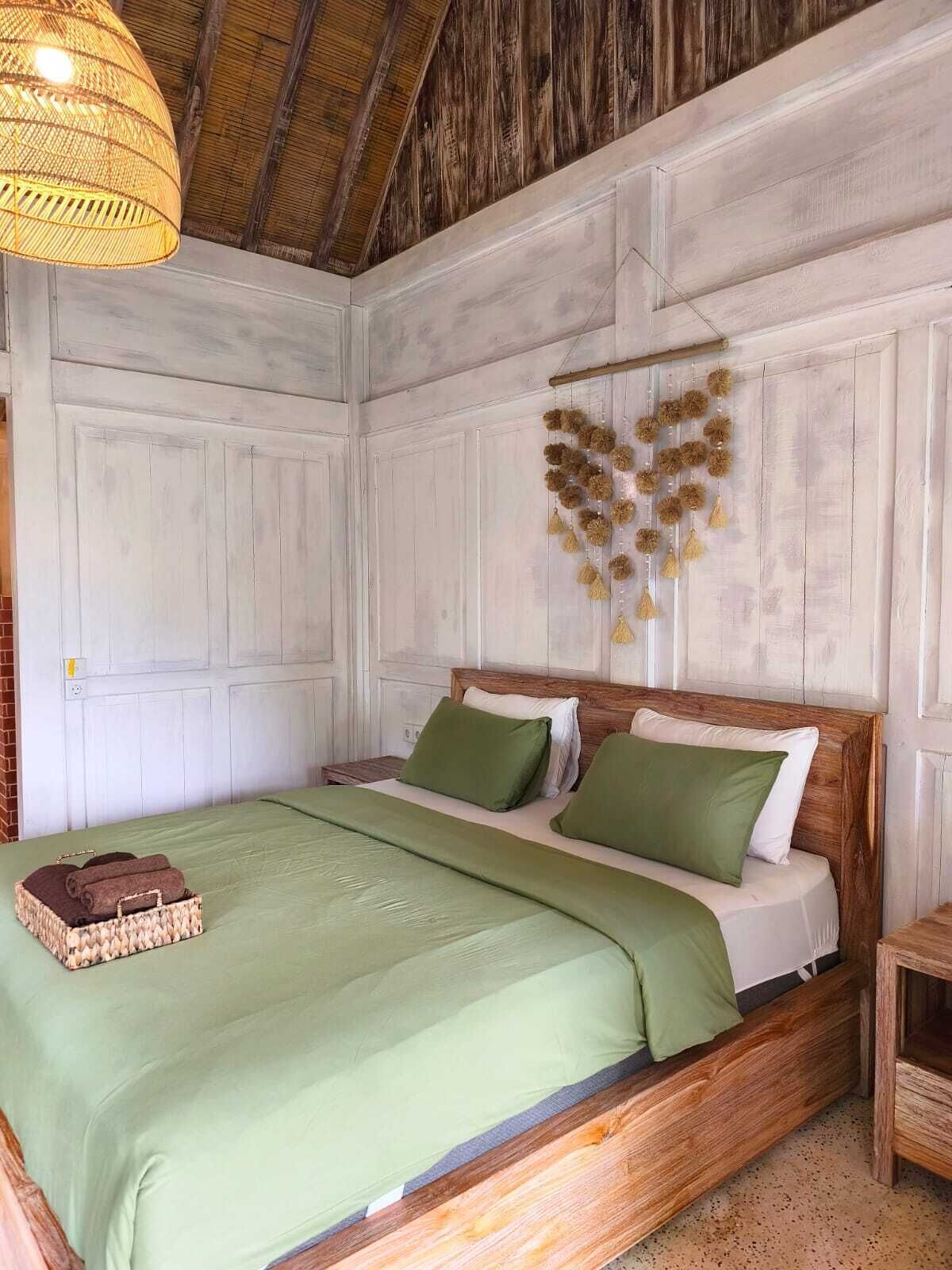 Una habitación con una cama de madera, ropa de cama verde, un adorno colgante y una cesta tejida.