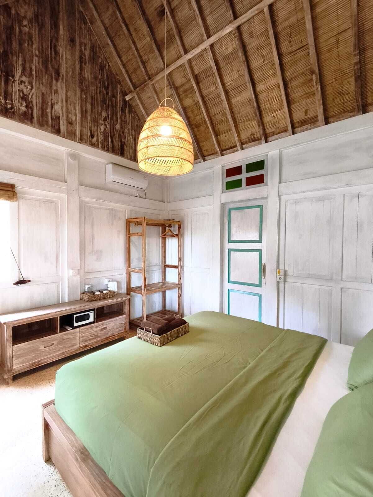 A room with a bed, a wooden dresser, a hanging light fixture, and a door with a green and red design.