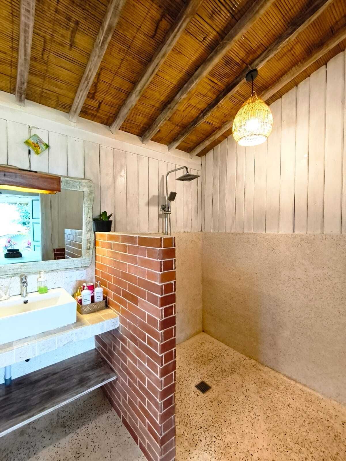 A bathroom with a shower, a sink, a mirror, and a hanging light fixture.