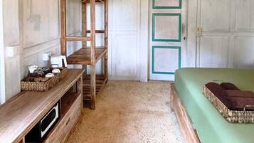 A room with a wooden ceiling, a bed with green bedding, a wooden bench, a shelf with items, and a door with green frames.