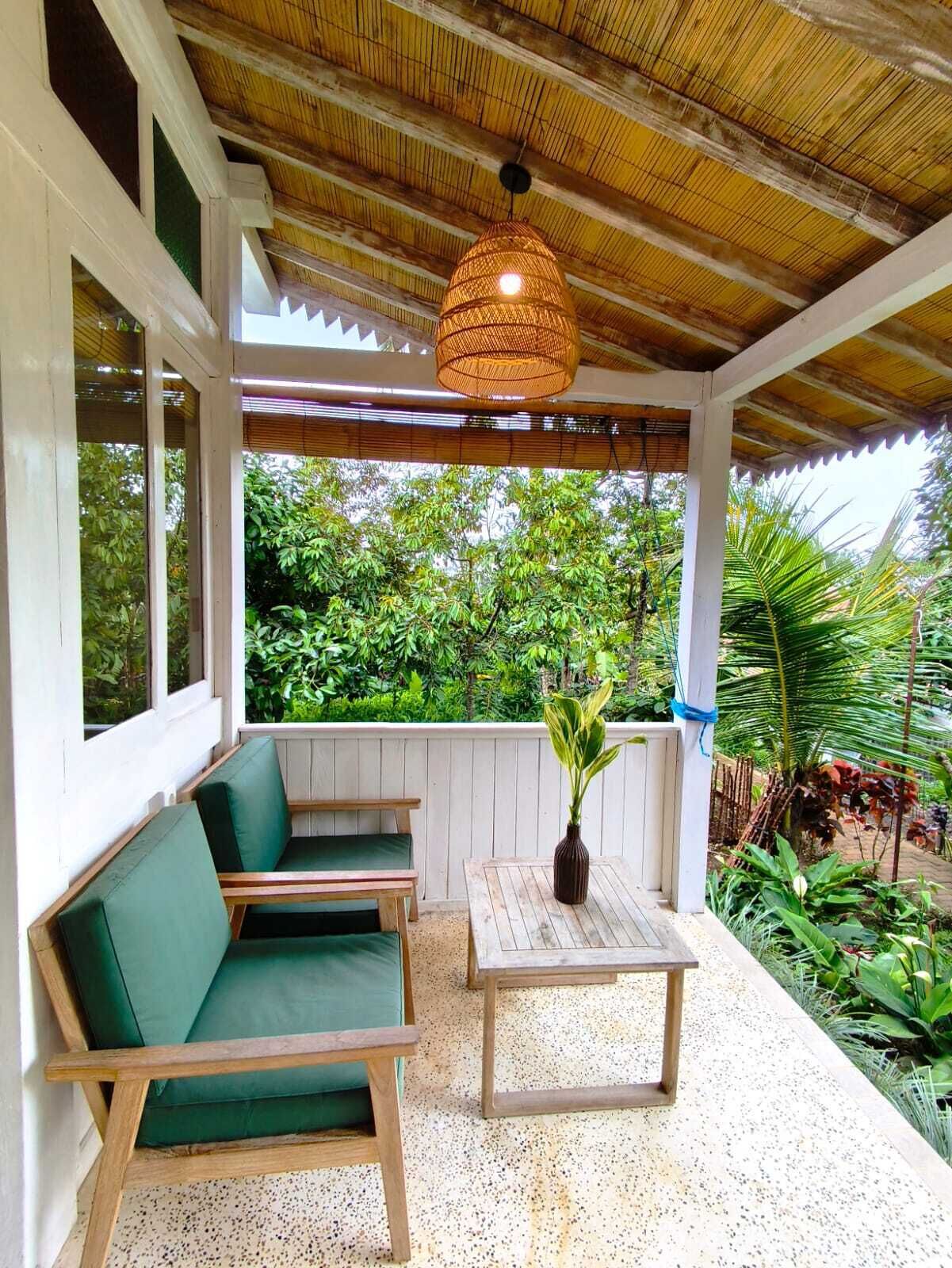 A covered outdoor seating area with a woven ceiling light, wooden furniture, and a view of lush greenery.
