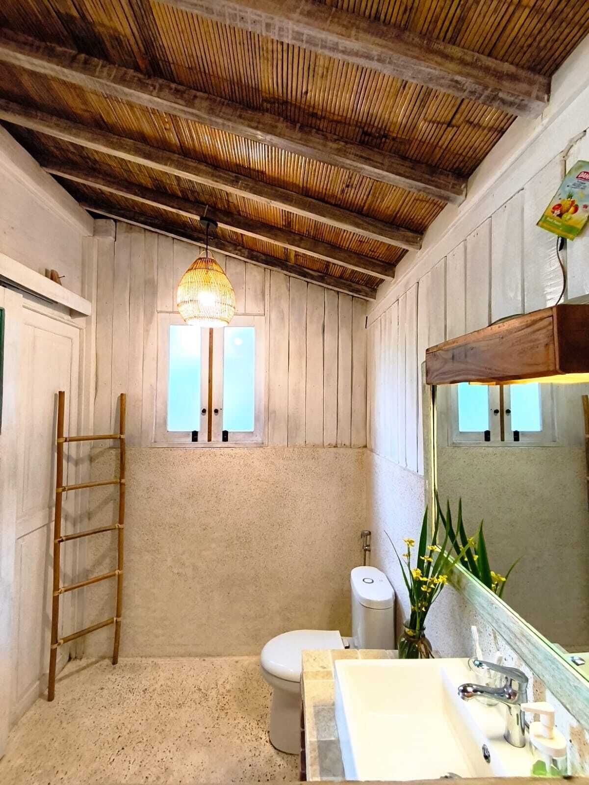 A bathroom with a wooden ceiling, a toilet, a sink with a mirror, and a hanging light fixture.