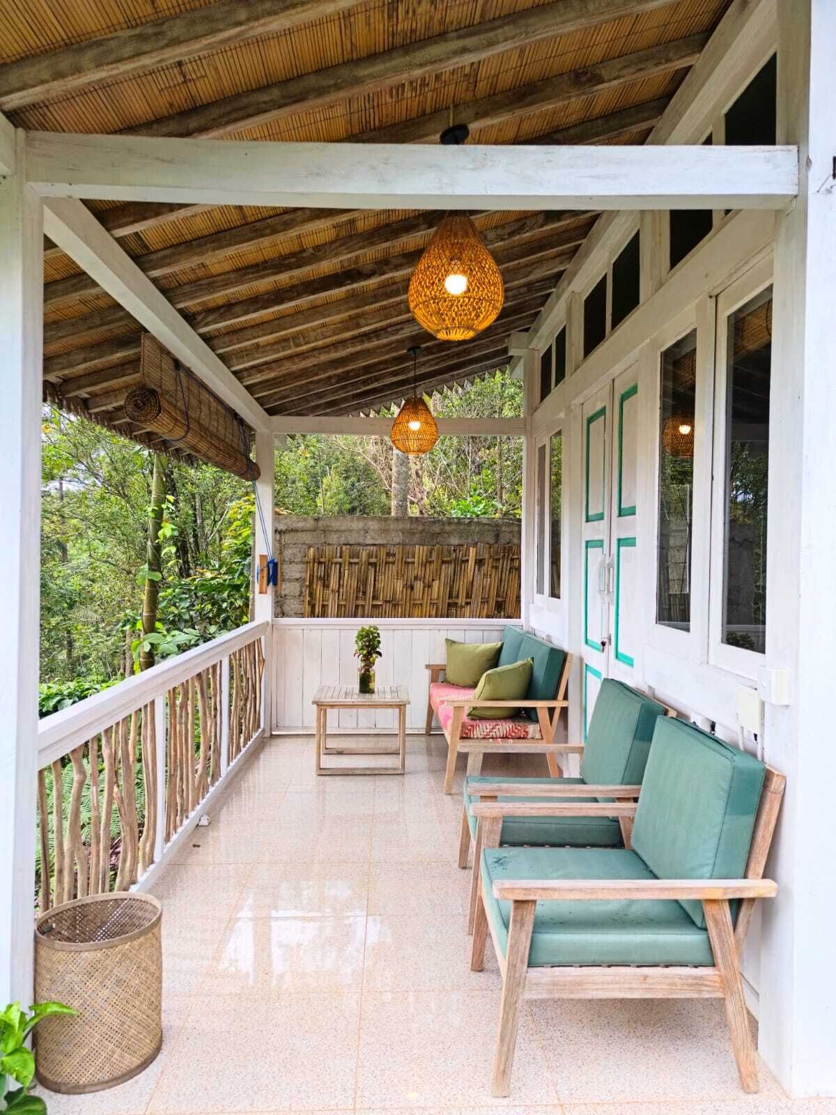 A covered porch with wooden furniture, a woven ceiling, and a view of greenery.
