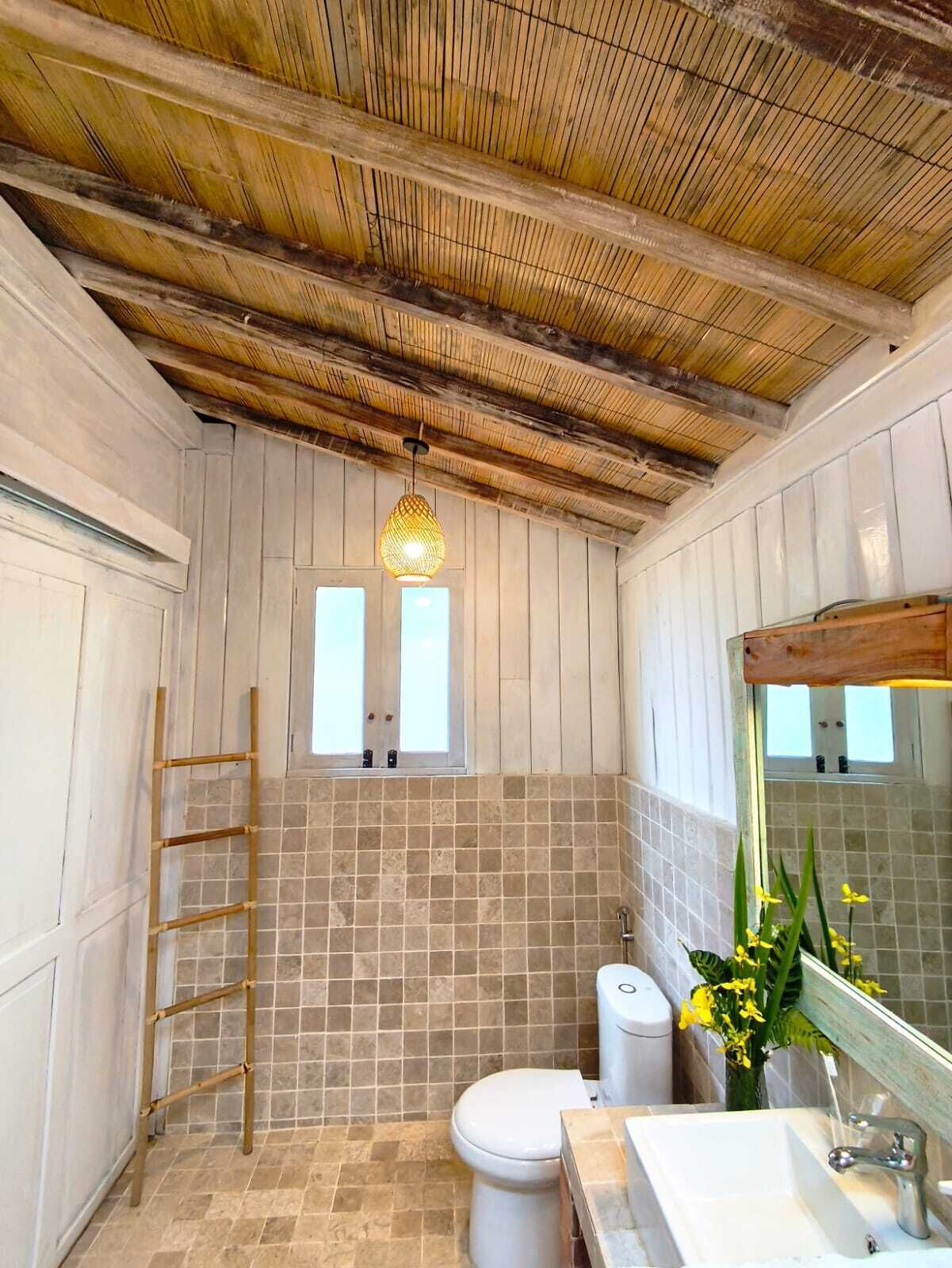 A bathroom with a wooden ceiling, tiled walls, a toilet, a sink, and a mirror.