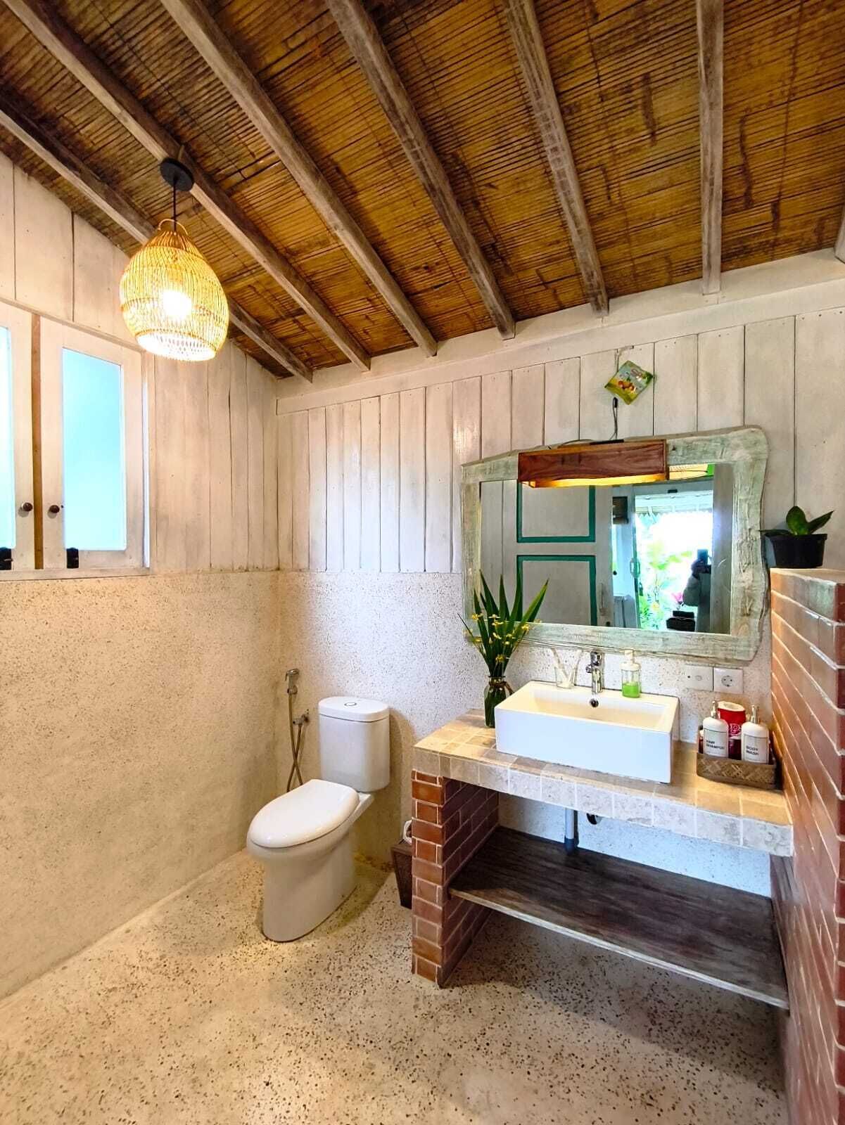 A bathroom with a white toilet, a sink with a mirror, a hanging light fixture, and a brick accent wall.
