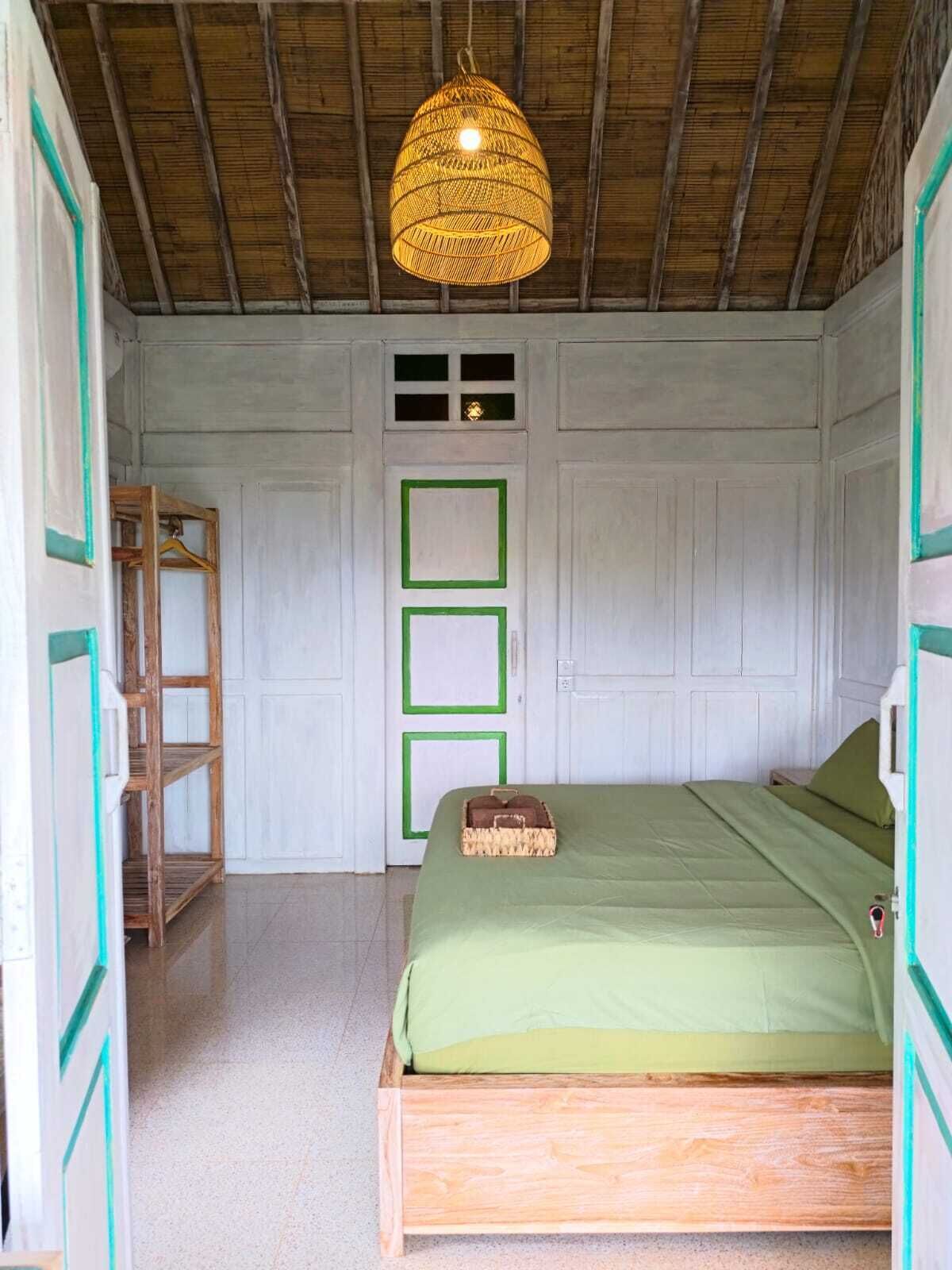 Una habitación con cama, lámpara colgante, escalera de madera y puerta con marcos verdes.