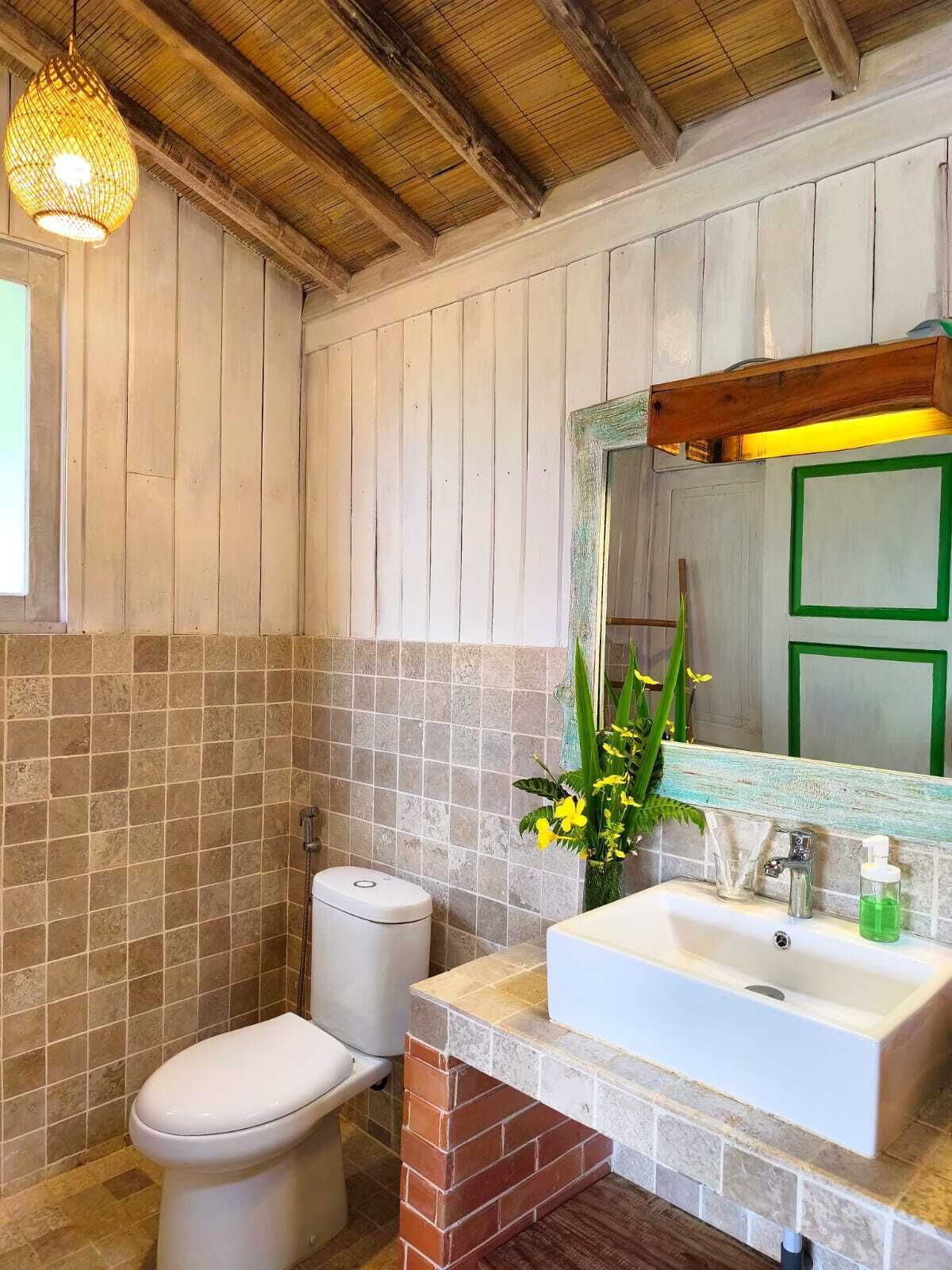 Une salle de bain avec des murs en bois, des toilettes blanches, un lavabo avec un miroir et un luminaire suspendu.
