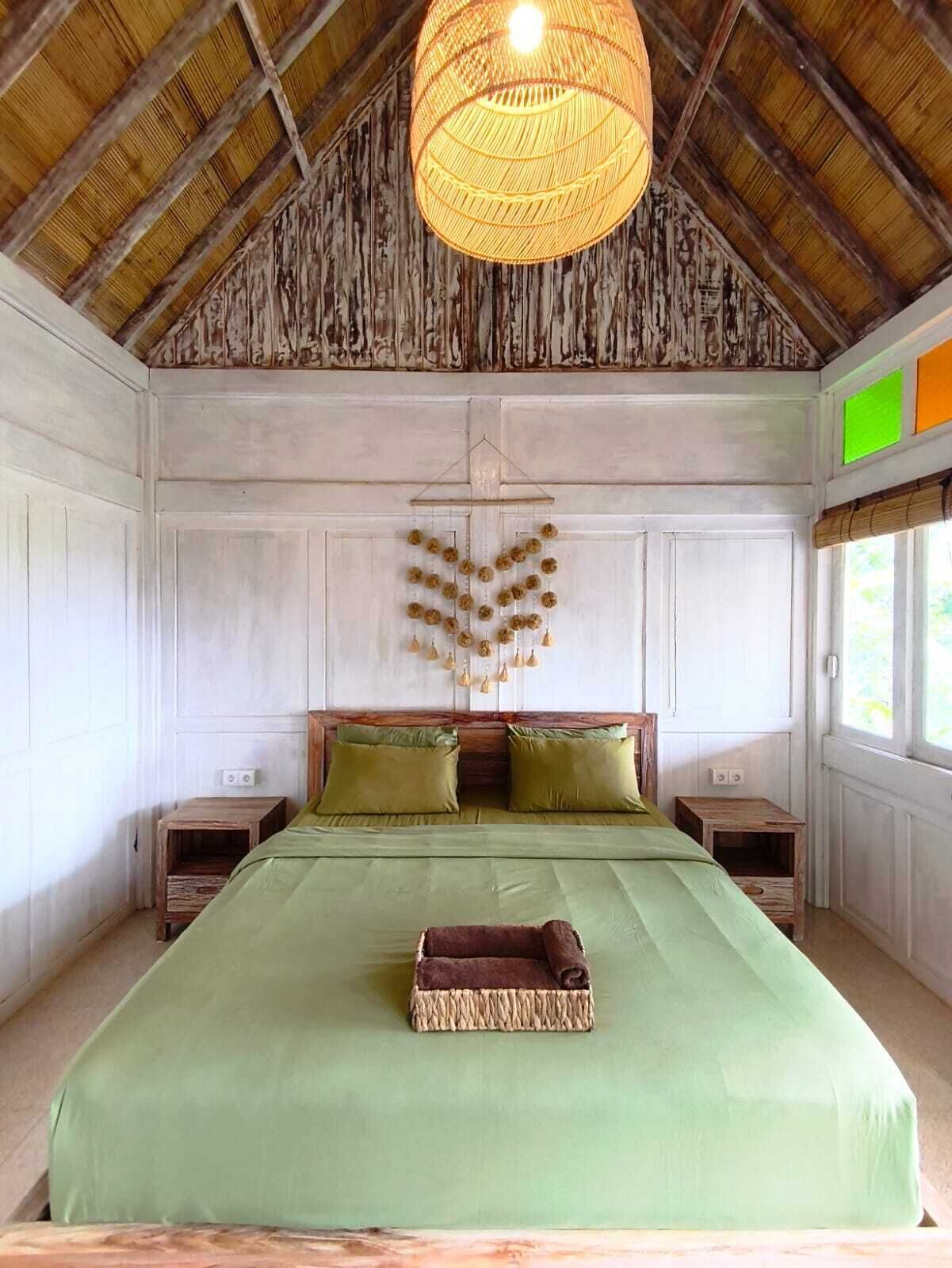 A room with a bed, wooden headboard, a hanging light fixture, and a window with blinds.