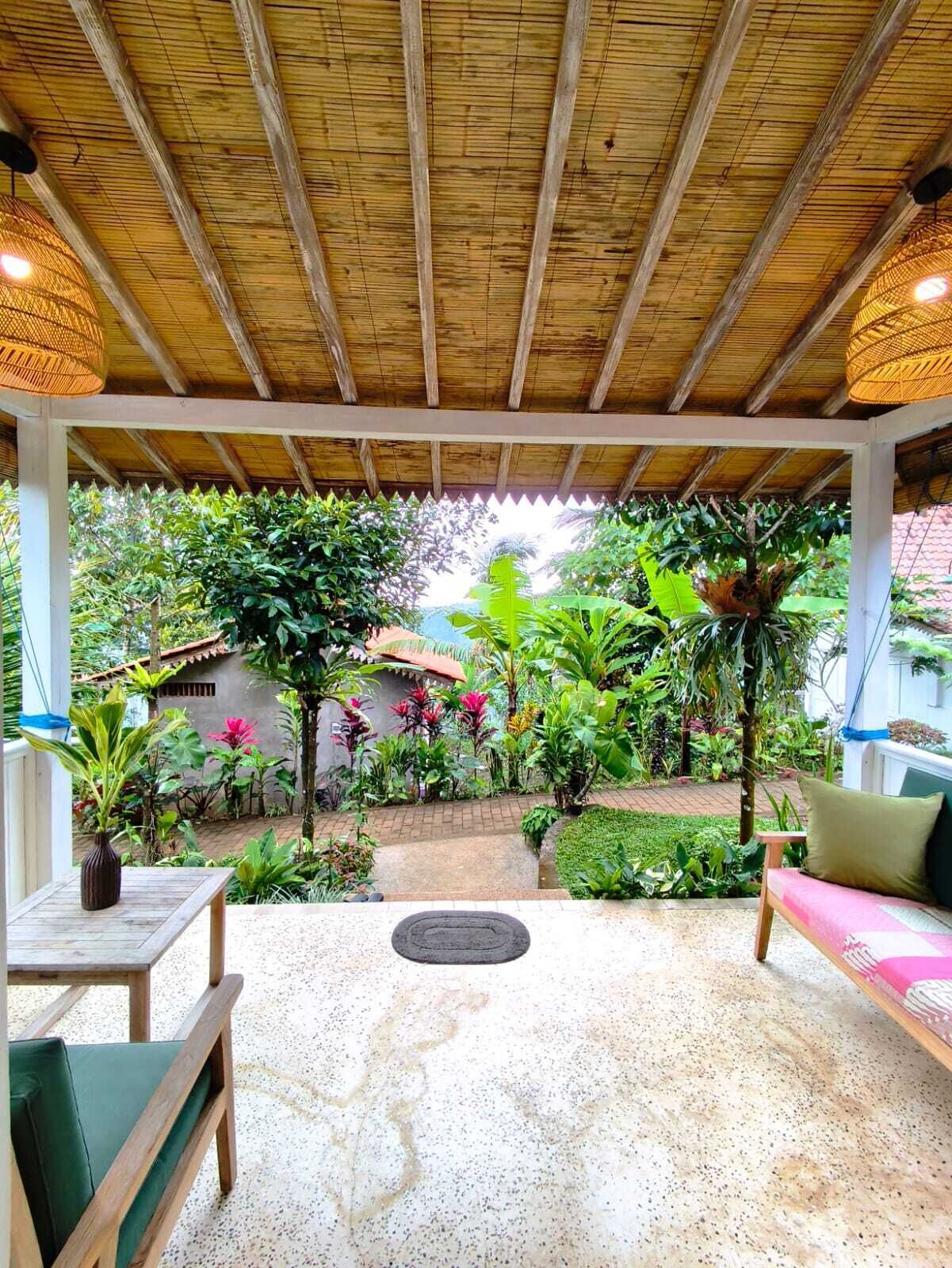 An outdoor patio with a wooden ceiling, a seating area with a bench and table, and a garden with various plants and a pathway.