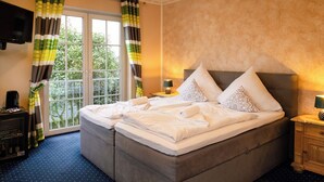Ein Doppelbett mit grauem Kopfteil, zwei Zierkissen, ein Nachttisch mit Lampe und ein Fenster mit Vorhängen.