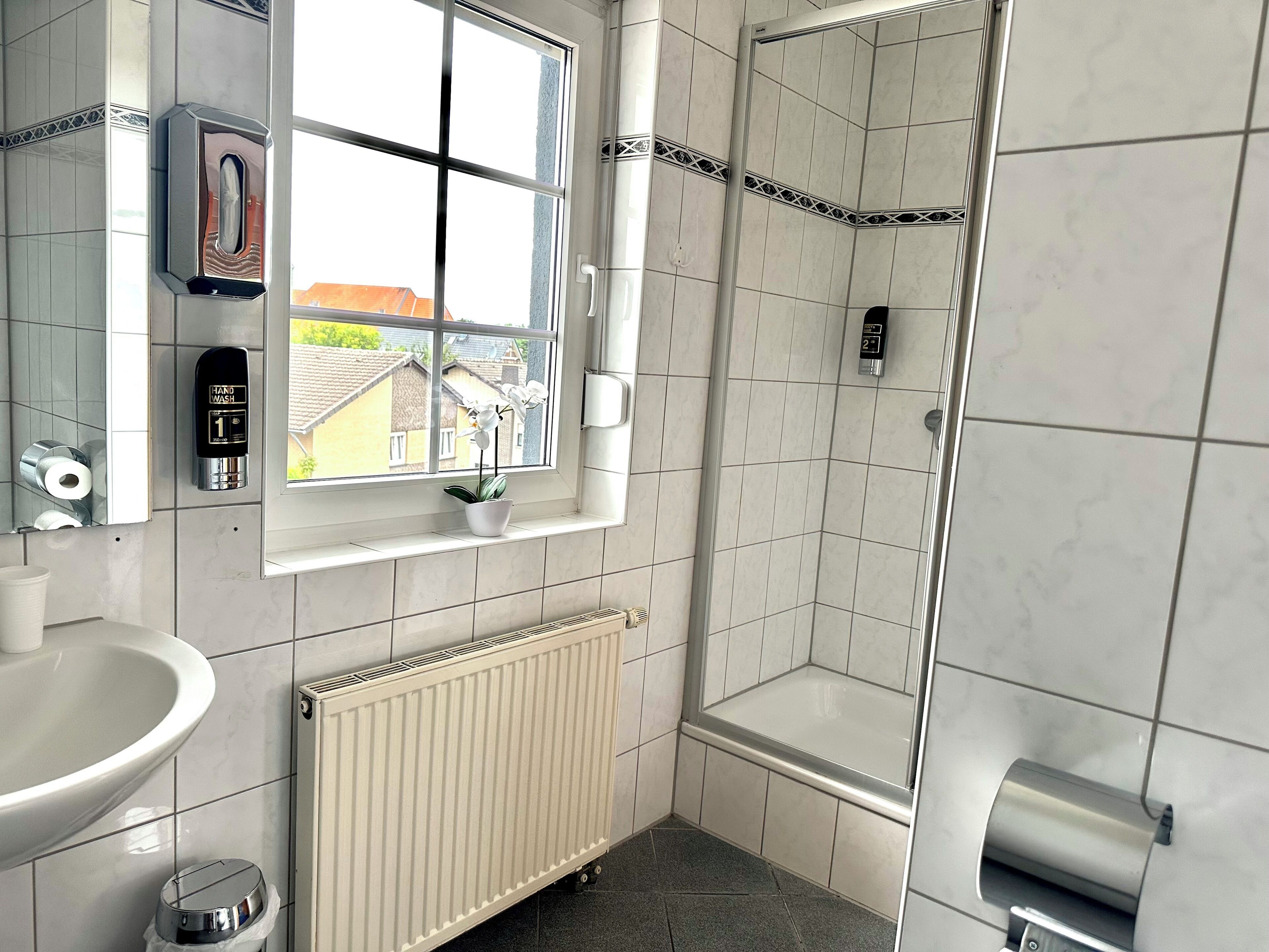 Een moderne badkamer met een wasbakje, een toiletpapierdispenser, een radiator en een raam met uitzicht op gebouwen.