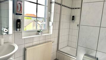 Een moderne badkamer met een wasbakje, een toiletpapierdispenser, een radiator en een raam met uitzicht op gebouwen.