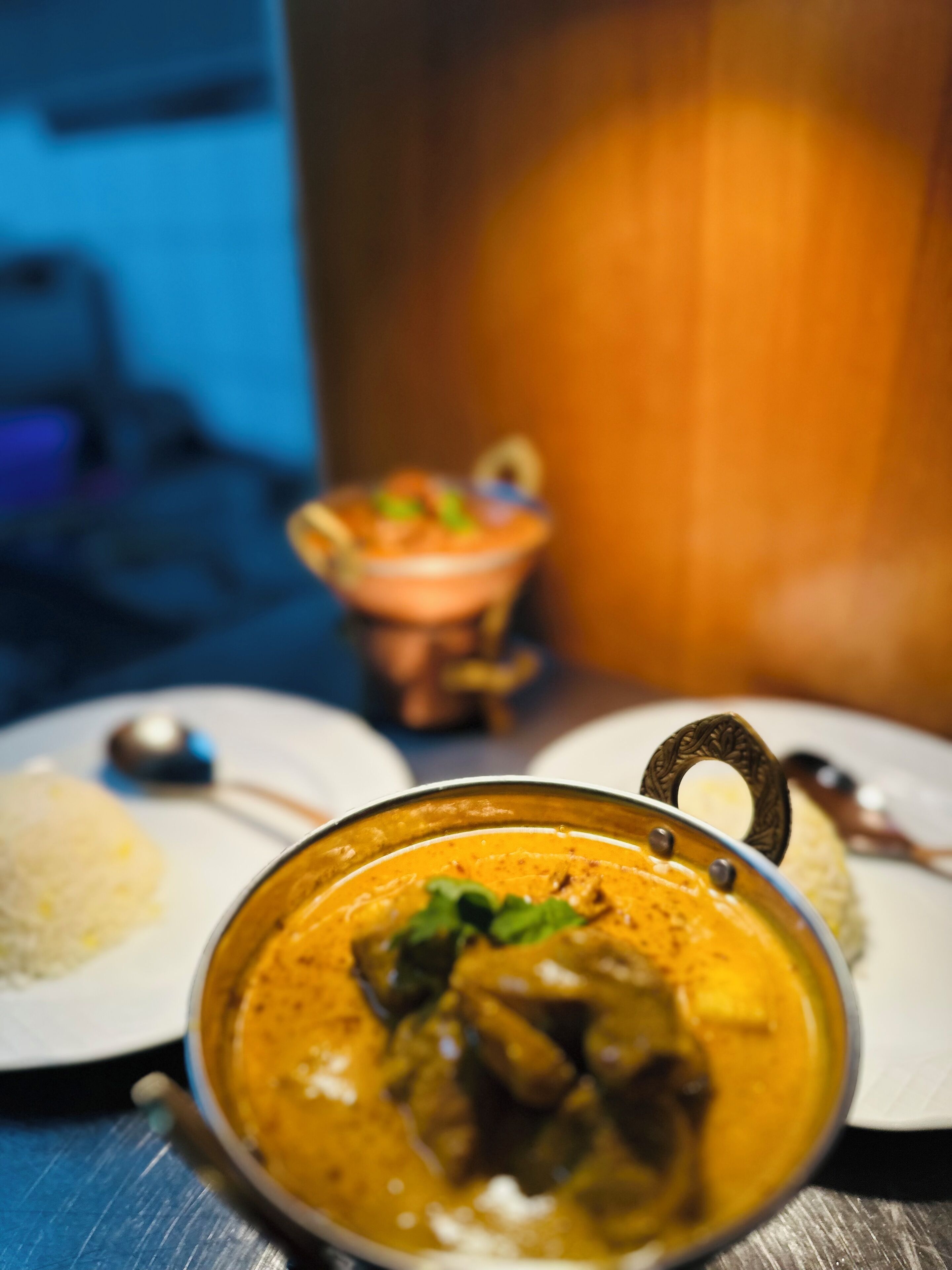 A close-up of a curry dish with a handle, accompanied by a plate of rice and a small bowl of salad.