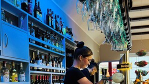 Eine Bar mit Regalen voller Spirituosen, einem Barkeeper, der Getränke zubereitet, und einer hängenden Leuchte.