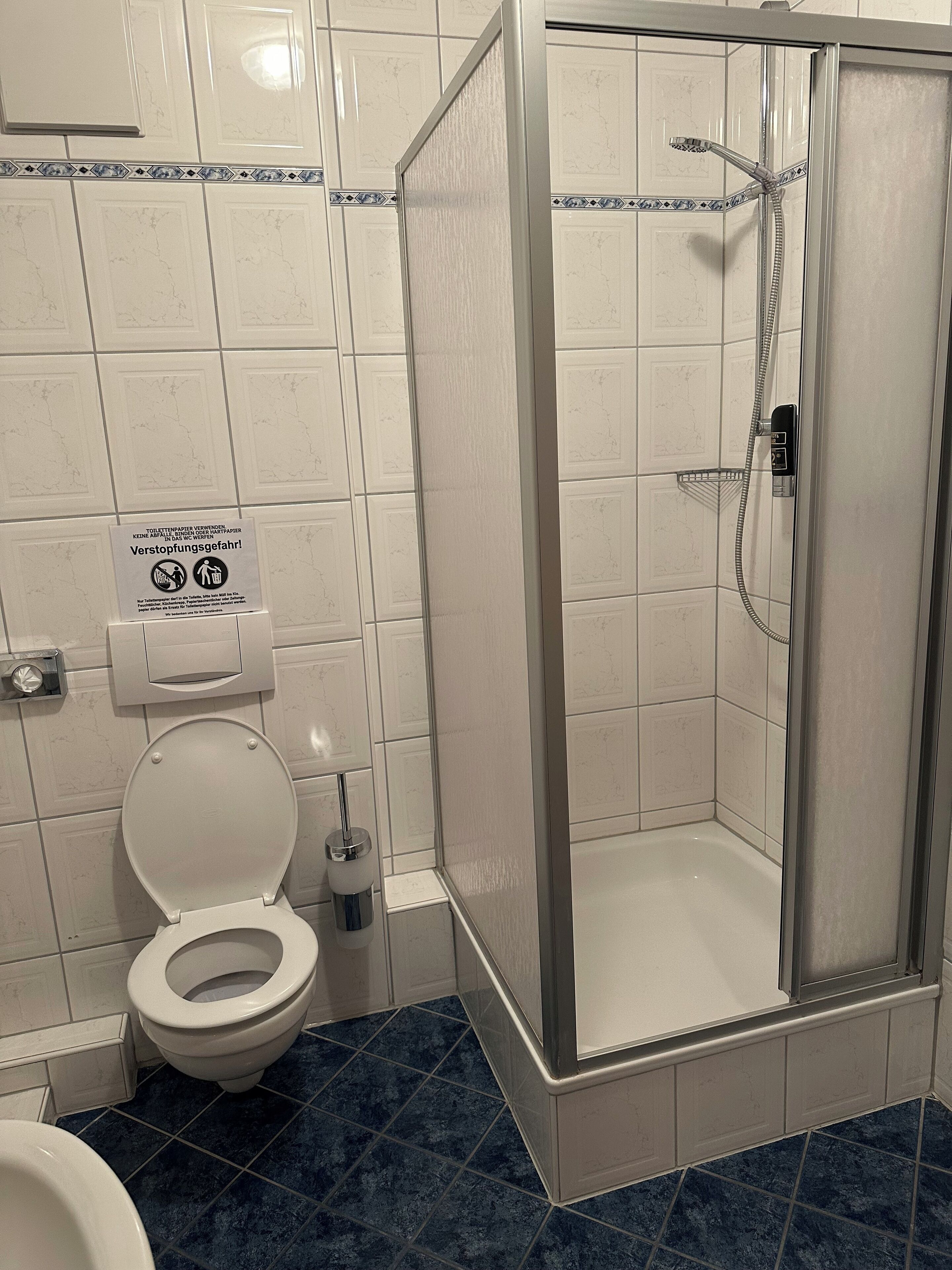 Un baño con inodoro, cabina de ducha y un cartel sobre el uso del papel higiénico.