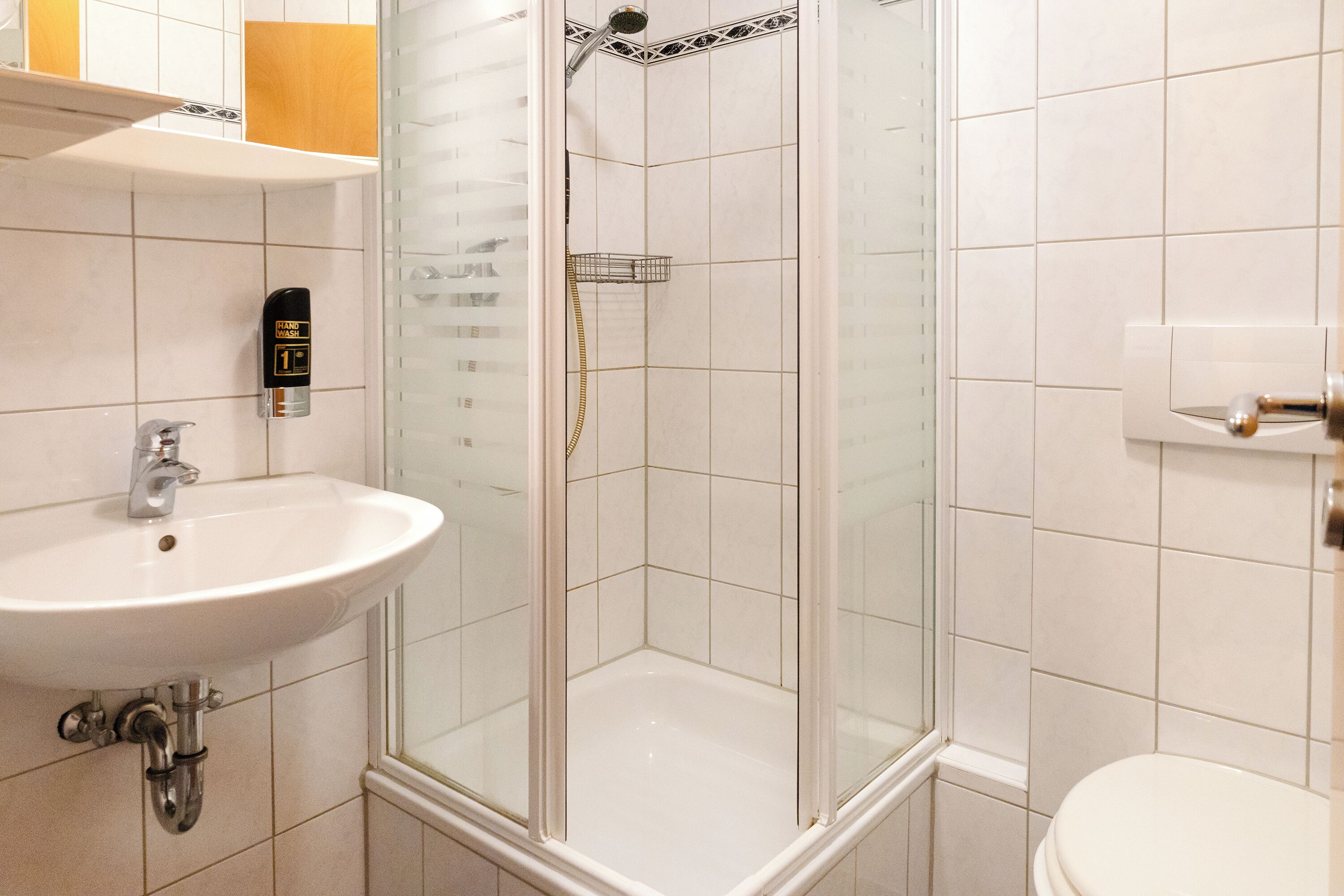Een badkamer met een wit wastafelmeubel, een douche met glazen wanden en een toilet.