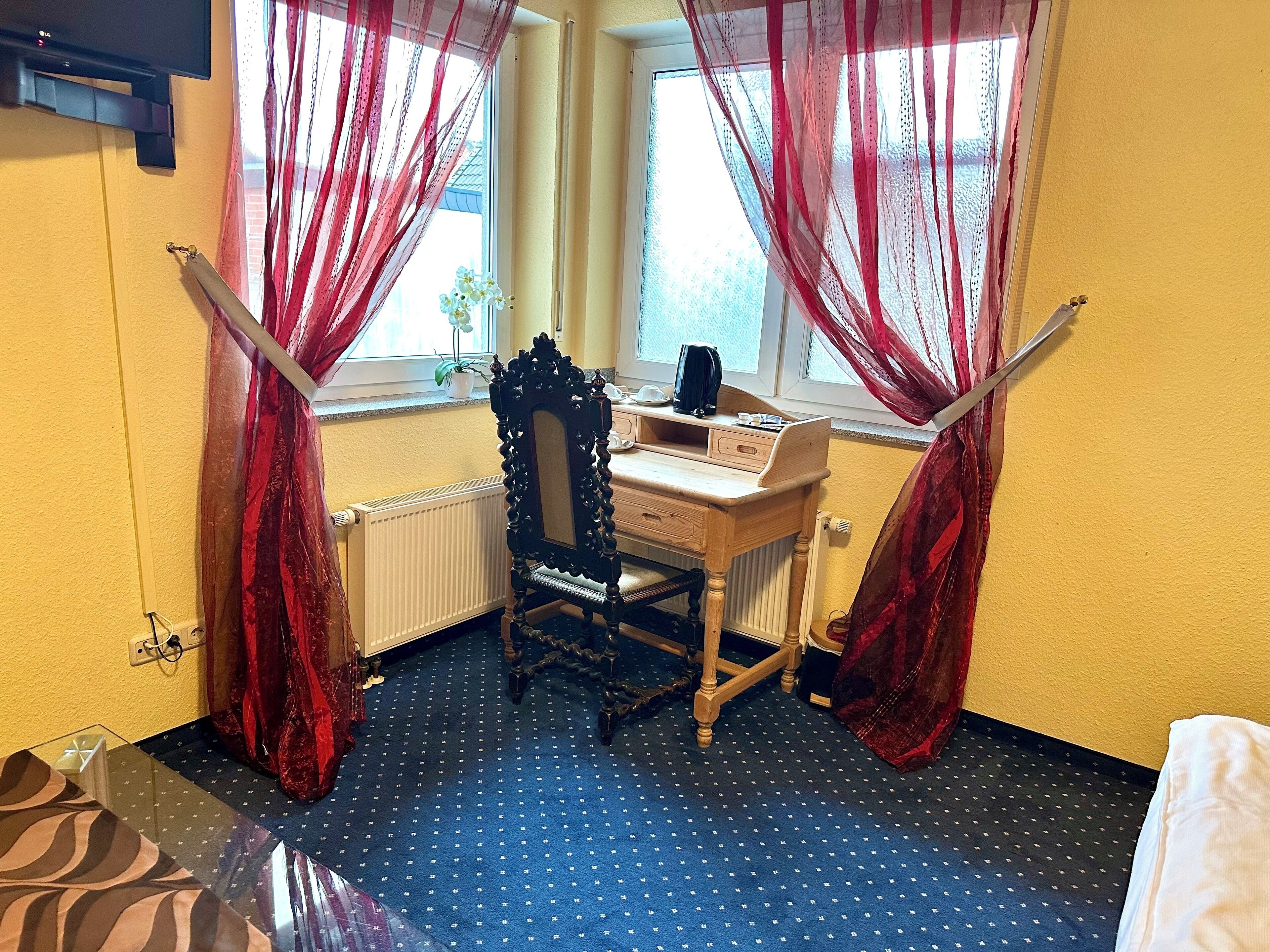 A room with a wooden desk, a chair, a radiator, and a window with red curtains.
