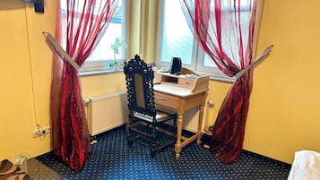 A room with a wooden desk, a chair, a radiator, and a window with red curtains.