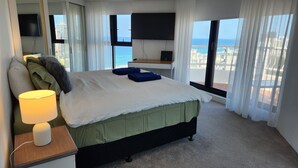 Quarto com cama, abajur, televisão e vista para o mar.