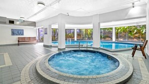 Um saguão de hotel com hidromassagem, piscina e grandes janelas com vista para áreas verdes.