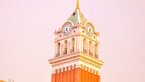 A clock tower with a clock on each side, surrounded by buildings with balconies. - S Gen Residences Phu Quoc (Phu Quoc)